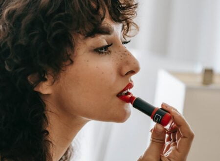 Young content woman applying red lipstick